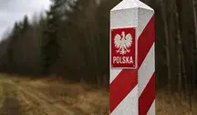Słupek graniczny w barwach biało-czerwonych stojący na skraju lasu, symbolicznie oznaczający granicę Polski na tle rozmytego, leśnego krajobrazu.