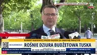 Mężczyzna, Przemysław Czarnek w garniturze udziela wypowiedzi mediom przed Kancelarią Prezesa Rady Ministrów w Warszawie. Na ekranie pasek informacyjny telewizji wPolsce24 dotyczący budżetu i polityki rządu Donalda Tuska