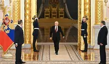 Władimir Putin przechodzi przez salę reprezentacyjną z dwoma wartownikami salutującymi, w tle złociste kolumny i rosyjska flaga państwowa