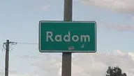 Zielona tablica drogowa z napisem ‘Radom’ przy drodze, w tle słup energetyczny i częściowo zachmurzone niebo