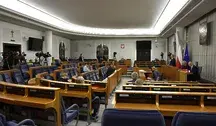 Sala Senatu RP z widokiem na miejsca senatorów, trybuny i sprzęt medialny; w tle flagi Polski i Unii Europejskiej oraz godło państwowe