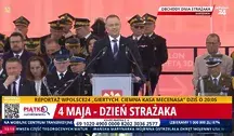 Prezydent Karol Nawrocki przemawia podczas obchodów Dnia Strażaka na placu w Warszawie. W tle widoczna grupa strażaków, w tym funkcjonariusze Państwowej Straży Pożarnej oraz wysokiej rangi wojskowi, z różnorodnymi odznaczeniami i mundurami. Na pierwszym planie widoczna jest scena z mikrofonem, a nad nią napis „Obchody Dnia Strażaka”. W tle czerwony baner z symbolem Polski