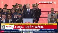 Prezydent Karol Nawrocki przemawia podczas obchodów Dnia Strażaka na placu w Warszawie. W tle widoczna grupa strażaków, w tym funkcjonariusze Państwowej Straży Pożarnej oraz wysokiej rangi wojskowi, z różnorodnymi odznaczeniami i mundurami. Na pierwszym planie widoczna jest scena z mikrofonem, a nad nią napis „Obchody Dnia Strażaka”. W tle czerwony baner z symbolem Polski