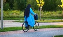 Siostra zakonna jedzie rowerem po ulicy wśród zieleni