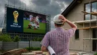 Mężczyzna na budowie w białym kasku patrzący na telebim