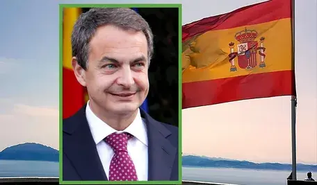 Były premier Hiszpanii José Luis Rodríguez Zapatero na tle hiszpańskiej flagi powiewającej nad wybrzeżem