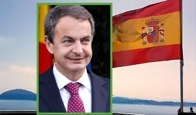 Były premier Hiszpanii José Luis Rodríguez Zapatero na tle hiszpańskiej flagi powiewającej nad wybrzeżem