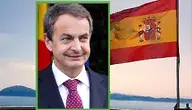 Były premier Hiszpanii José Luis Rodríguez Zapatero na tle hiszpańskiej flagi powiewającej nad wybrzeżem