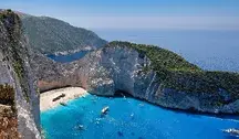 Plaża Navagio (Shipwreck Beach) na wyspie Zakynthos w Grecji, z turkusową wodą, białym piaskiem, słynnym wrakiem statku Panagiotis i stromymi klifami otaczającymi zatokę, widziana z perspektywy klifu.