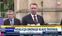 Przemysław Czarnek podczas konferencji prasowej przed budynkiem, udzielający wypowiedzi mediom, z widocznymi mikrofonami stacji telewizyjnych oraz paskiem informacyjnym na ekranie dotyczącym polityki gospodarczej i klasy średniej w Polsce.