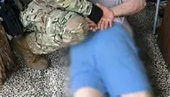 Funkcjonariusz CBŚP w umundurowaniu taktycznym obezwładnia zatrzymanego mężczyznę leżącego na podłodze w mieszkaniu.