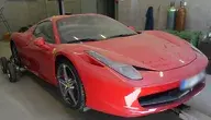 Czerwone Ferrari zabezpieczone przez policję, ustawione w warsztacie na wózkach transportowych, z zamazanymi elementami nadwozia i widocznymi napisami na masce.