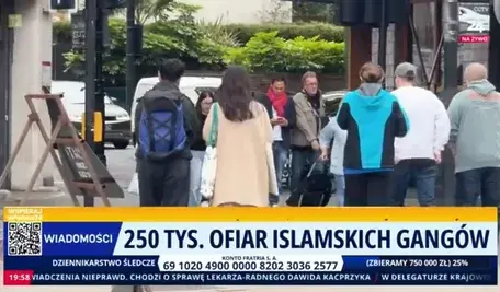 Ujęcie z ulicy przedstawiające grupę przechodniów na chodniku w mieście. Na dole ekranu widoczny pasek informacyjny programu telewizyjnego z napisem „250 tys. ofiar islamskich gangów” oraz elementami graficznymi stacji informacyjnej.