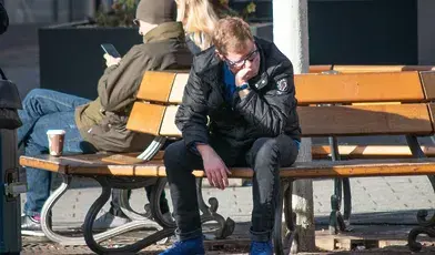 Zrezygnowany młody mężczyzna siedzi na ławce w mieście, z głową opartą na dłoni, ilustrując problem bezrobocia i rosnących długów wśród młodych Polaków