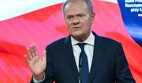 Premier w trakcie konferencji prasowej, gestykulujący podczas wypowiedzi dotyczącej relacji Polski z Ukrainą, na tle biało-czerwonej flagi.