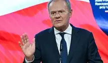 Premier w trakcie konferencji prasowej, gestykulujący podczas wypowiedzi dotyczącej relacji Polski z Ukrainą, na tle biało-czerwonej flagi.