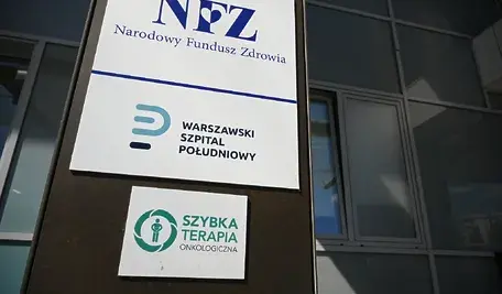 Zewnętrzna tablica informacyjna Narodowego Funduszu Zdrowia oraz Warszawskiego Szpitala Południowego umieszczona na elewacji budynku. Widoczne są także oznaczenia szybkiej terapii onkologicznej, wskazujące na działalność placówki w zakresie leczenia pacjentów onkologicznych.