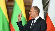 Donald Tusk podczas wystąpienia publicznego na konferencji, gestykulujący uniesionym palcem w trakcie przemówienia. W tle widoczne są flagi Polski i Litwy, sugerujące kontekst spotkania międzynarodowego lub dwustronnych rozmów.