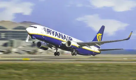 Samolot Ryanair w trakcie startu z pasa startowego, uchwycony w dynamicznym momencie wznoszenia się maszyny nad lotniskiem. W tle widoczna infrastruktura terminala oraz niebo z lekkim zachmurzeniem, co podkreśla ruch i intensywność operacji lotniczych. Ujęcie ilustruje kontekst działalności przewoźnika w segmencie tanich lotów, gdzie kluczową rolę odgrywa szybka rotacja i wysoka intensywność operacyjna.
