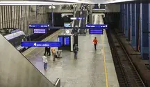 Pasażerowie na peronie stacji kolejowej, widok na tory, schody ruchome i rozkłady jazdy – ilustracja problemów z punktualnością pociągów w Polsce.