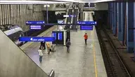 Pasażerowie na peronie stacji kolejowej, widok na tory, schody ruchome i rozkłady jazdy – ilustracja problemów z punktualnością pociągów w Polsce.