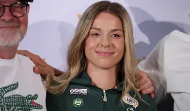 Maja Chwalińska podczas konferencji prasowej, ubrana w strój tenisowy z logo Roland Garros i sponsorów Oshee oraz Lotto, uśmiecha się do kamery