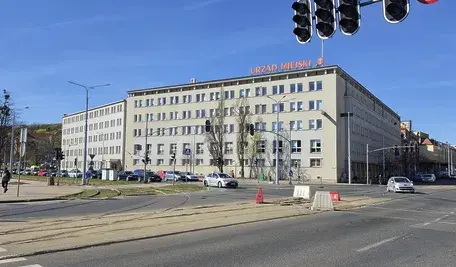 Budynek Urzędu Miejskiego w Gdańsku przy ruchliwej ulicy, widok z perspektywy skrzyżowania z sygnalizacją świetlną i tramwajowymi torami