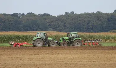 Dwa zielone ciągniki pracujące na polu — ilustracja artykułu o dopłatach do nawozów dla rolników.