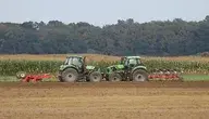 Dwa zielone ciągniki pracujące na polu — ilustracja artykułu o dopłatach do nawozów dla rolników.