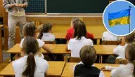 Uczniowie siedzący w ławkach podczas lekcji i umieszczona w górnym rogu flaga Ukrainy