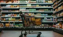 Wózek sklepowy w supermarkecie na tle półek pełnych produktów spożywczych, symbolizujący zakupy żywności w sklepie.