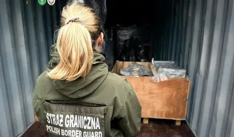 Funkcjonariuszka Straży Granicznej kontroluje zawartość kontenera z drewnianymi skrzyniami i pakunkami podczas operacji przechwycenia narkotyków ukrytych w ładunku.