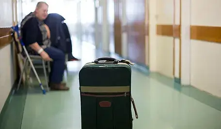 Walizka stojąca na korytarzu szpitalnym, w tle siedzi pacjentka