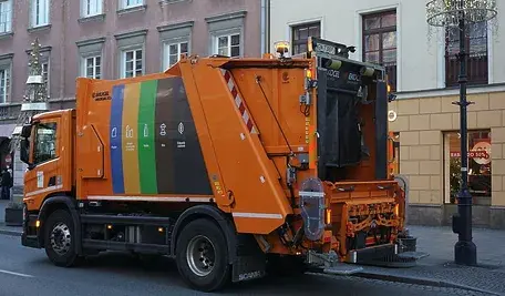 Pomarańczowa śmieciarka jadąca ulicami Warszawy