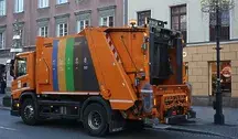 Pomarańczowa śmieciarka jadąca ulicami Warszawy