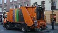 Pomarańczowa śmieciarka jadąca ulicami Warszawy