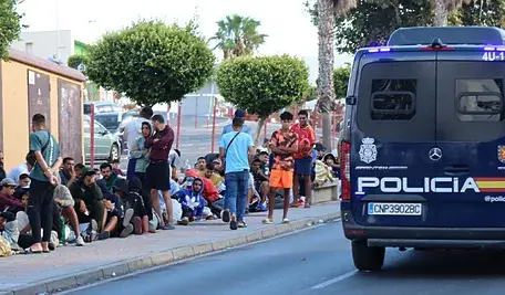 Radiowóz hiszpańskiej policji w Ceucie obok grupy migrantów oczekujących przy ulicy podczas napiętej sytuacji bezpieczeństwa