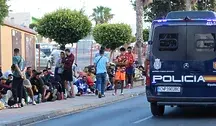 Radiowóz hiszpańskiej policji w Ceucie obok grupy migrantów oczekujących przy ulicy podczas napiętej sytuacji bezpieczeństwa