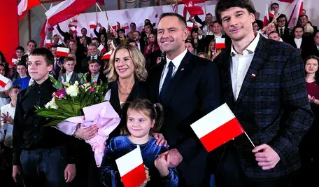 Karol Nawrocki z rodziną podczas uroczystości z polskimi flagami w tle.