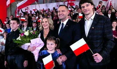 Karol Nawrocki z rodziną podczas uroczystości z polskimi flagami w tle.