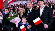 Karol Nawrocki z rodziną podczas uroczystości z polskimi flagami w tle.
