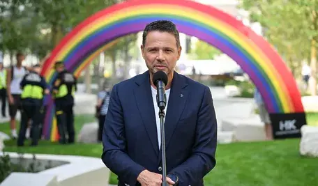 Rafał Trzaskowski podczas wystąpienia w Warszawie przy mikrofonie, w tle kolorowy łuk symbolizujący wydarzenie miejskie