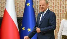 Donald Tusk w garniturze podczas oficjalnego wystąpienia, w tle widoczne flagi Polski i Unii Europejskiej. Zdjęcie ilustruje polityczny konflikt między premierem a prezydentem Karolem Nawrockim dotyczący reform, ustaw i bezpieczeństwa państwa.