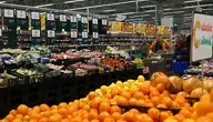 Sklepowe stoisko z produktami spożywczymi – na półkach pieczywo, nabiał, słodycze. Wyraźnie widoczne metki z cenami, niektóre z przekreślonymi starymi kwotami i nowymi, wyższymi. Ilustracja codziennej rzeczywistości zakupów Polaków w czasach inflacji.