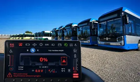Zajezdnia autobusowa w Chełmie z kilkoma zaparkowanymi wodorowymi autobusami. Na zdjęcie nałożono grafikę symbolu baterii z poziomem naładowania 0%. Ilustracja problemów z awaryjnością i gotowością wodorowego taboru.