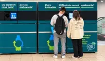 Dwoje młodych ludzi oddaje plastikowe butelki do dużego, niebiesko-zielonego butelkomatu w markecie Lidl