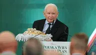 Jarosław Kaczyński w ciemnym garniturze stoi za białą mównicą z napisem „Polska Wieś Polski Plan”. Przed nim leży tradycyjny, ozdobny bochenek chleba na serwecie. W tle widoczna zielona ścianka z grafiką.