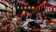 Dramatyczna, fotorealistyczna grafika w formacie poziomym przedstawiająca rosnące koszty życia. Po lewej stronie znajduje się supermarketowa półka z podstawowymi produktami oraz duży wózek sklepowy wypełniony żywnością. W centrum widać zmartwioną parę siedzącą przy stole, przeglądającą rachunki i dokumenty. Przed nimi leży pusty portfel, kilka monet oraz rozrzucone paragony. W tle widoczny jest czerwony wykres symbolizujący wzrost cen, stosy monet, miejskie osiedle i polska flaga w ciemnej, dramatycznej scenerii. Na stole znajduje się kubek z czerwonym symbolem serca. Całość utrzymana jest w mrocznym, alarmującym stylu przedstawiającym presję finansową i wzrost kosztów codziennego życia.