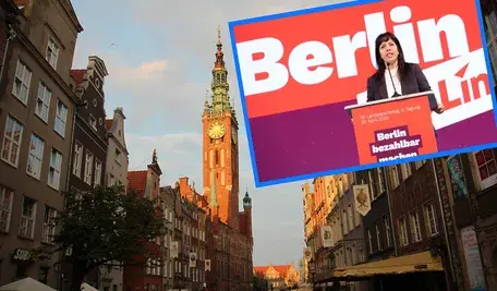 Fotomontaż przedstawiający ulicę Długi Targ oraz Ratusz Głównego Miasta w Gdańsku. Na tło polskiej architektury nałożona jest przekrzywiona grafika z wizerunkiem niemieckiej polityk Elif Eralp z partii Die Linke, przemawiającej na tle haseł "Berlin" oraz "Berlin bezahlbar machen"