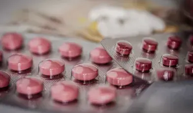 alt="Tabletki w blistrach farmaceutycznych na tle banknotów, ilustracja do tematu wyłudzeń refundacji leków z NFZ"